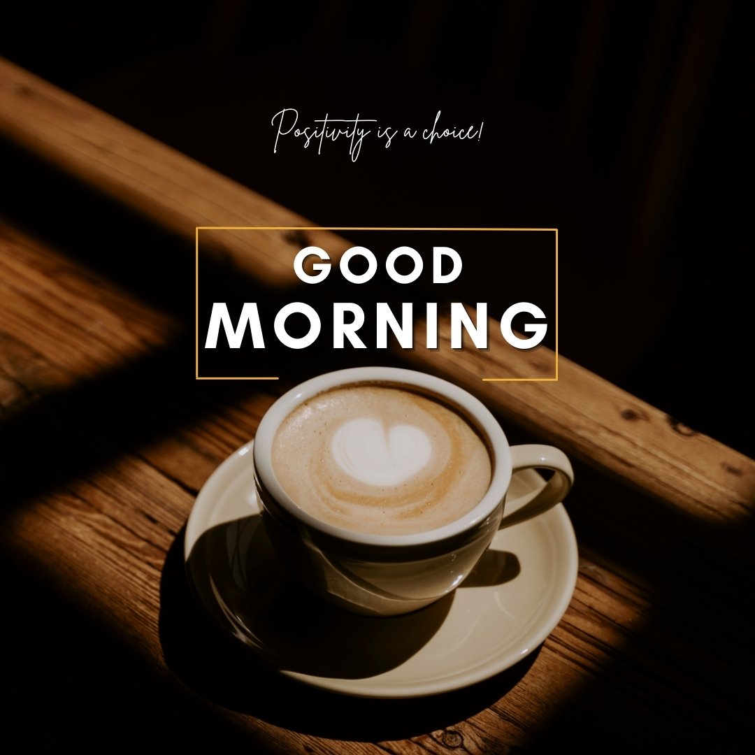 A cup of coffee with latte art sits on a wooden table in a dimly lit setting. The text overlay reads, "Good Morning. Positivity is a choice!" This image is a stylish representation of good morning coffee images.